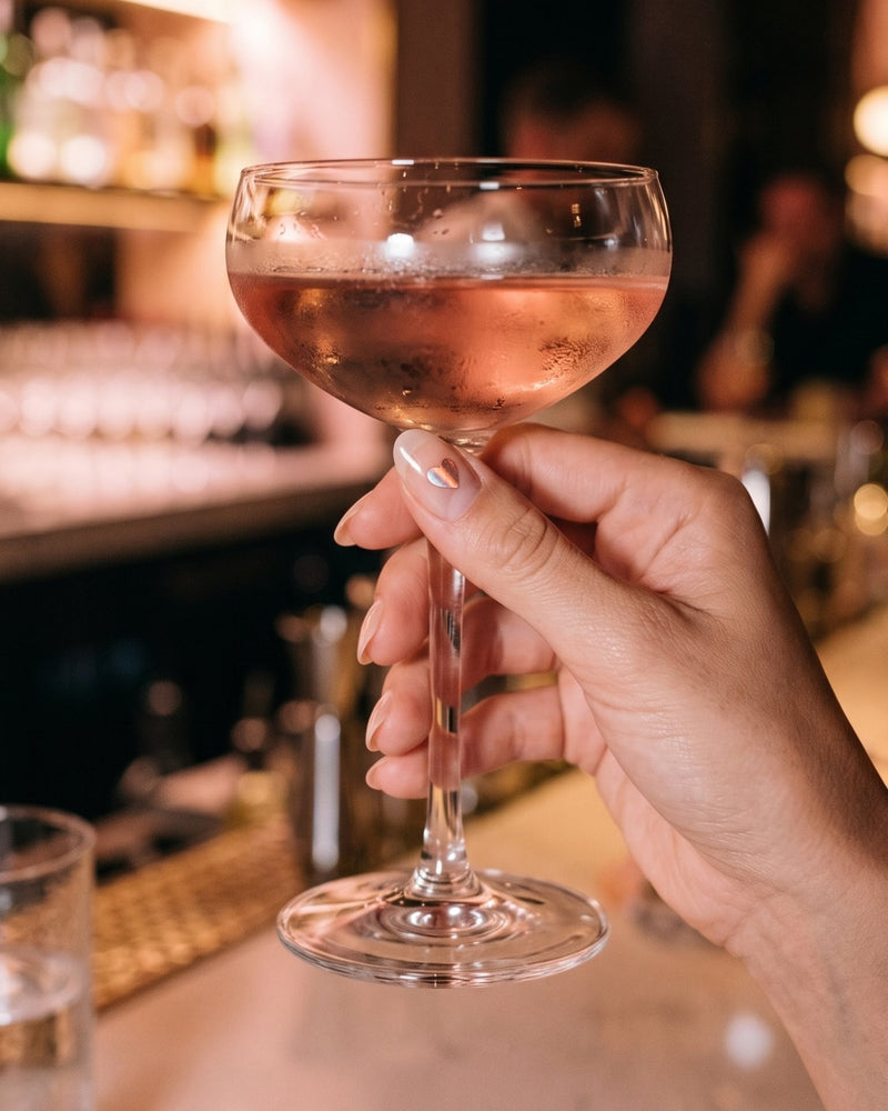 Main avec un cocktail et un autocollant NightNail